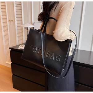 Détail latéral d'un grand sac cabas noir avec texte en relief et bandoulière longue