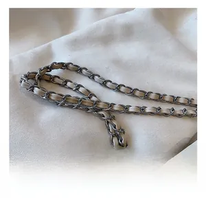 Close-up of polished silver metal chain interwoven with beige leather on crossbody bag