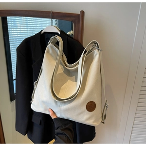 Détail d'un grand cabas en toile blanc cassé avec écusson rond en cuir et large bandoulière