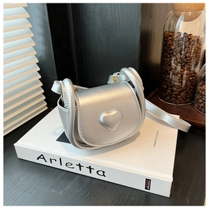 Close-up of silver mini saddle bag with a 3D heart detail and metallic leather texture