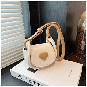 Detail view of a cream saddle bag with a brown heart accent and natural window light