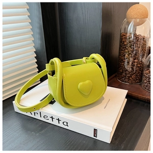 Detail of a neon green heart-shaped crossbody bag on a white book with coffee beans