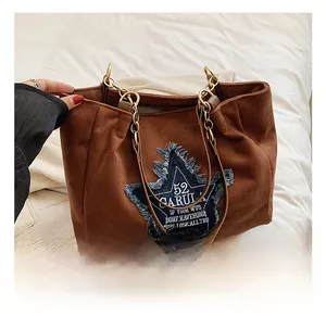 Detail of brown suede tote bag with blue denim star patch and gold chain strap