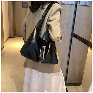 Détail d'un grand sac hobo noir en cuir huilé brillant porté par un mannequin pour le travail