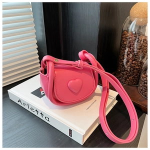 Detail of pink saddle bag featuring a 3D heart ornament and adjustable knotted strap