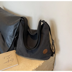 Détail d'un sac cabas en toile noire avec logo en cuir marron et bandoulière réglable