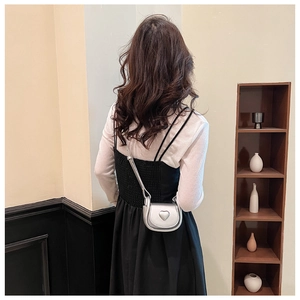Detail of silver mini crossbody bag with heart relief on a model in a stylish interior