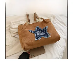 Detail view of large brown suede tote bag with denim star and size reference phone