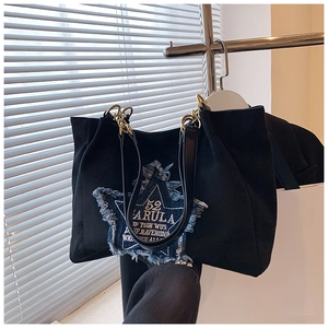 Detail of black tote bag featuring denim star patch and golden metal chain strap
