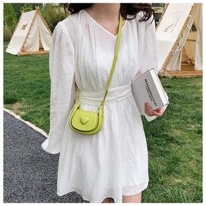 Outdoor shot of lime green mini crossbody bag with heart detail on a white summer dress