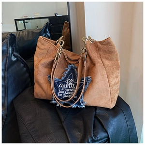 Close-up of brown suede tote bag with denim star patch and gold metal chain strap