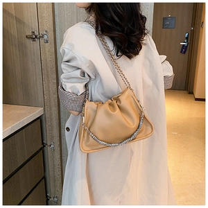 Detail of khaki pleated cloud bag with dual chain straps worn by model in a hallway