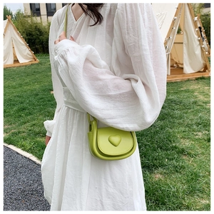 Light green mini saddle bag with heart detail worn by a model in an outdoor setting
