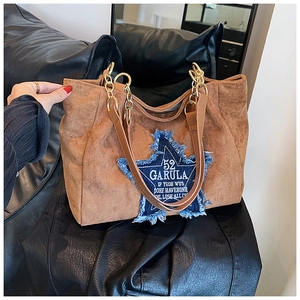 Close-up of brown suede tote bag with large blue denim star patch and gold chain strap