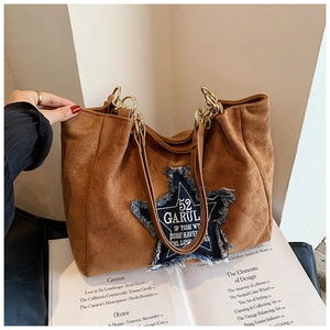 Detail of brown suede tote bag featuring a blue denim star patch and gold hardware