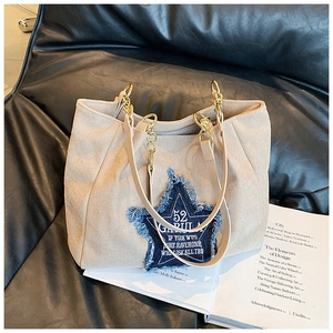 Detail of a large tote bag with denim star patch and gold chain handles on a sofa