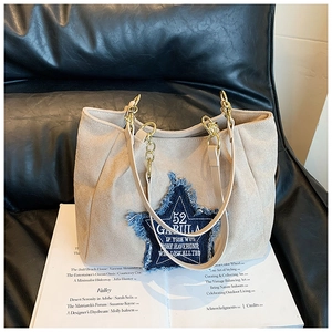 Detail of beige tote bag featuring a denim star patch and gold chain strap on a magazine