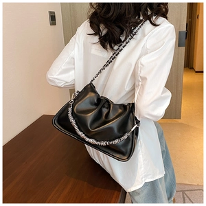 Close-up of black pleated cloud bag with chunky silver chain strap worn by a model