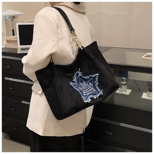 Detail of black tote bag featuring a denim star patch and gold chain leather strap