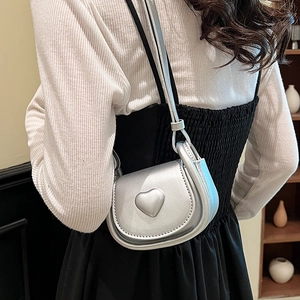 Chic silver metallic mini saddle bag with heart detail shown on a female model