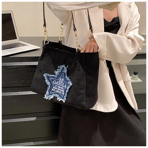 Detail of black suede tote bag featuring denim star patch and gold chain leather strap