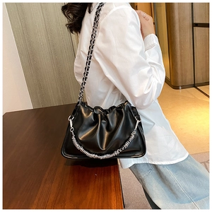 Detail of black pleated cloud bag featuring silver chain strap on a wooden surface