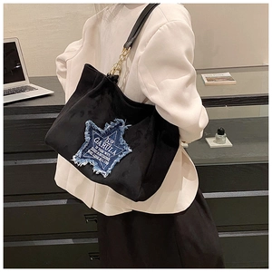 Detail of black matte tote bag featuring a denim star patch and gold chain strap