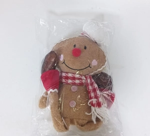 Detail of gingerbread plush doll with chef hat and plaid scarf in plastic packaging