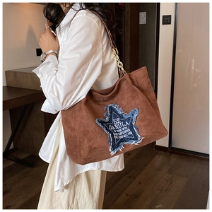 Close-up of large brown tote bag featuring a denim star patch and gold chain strap
