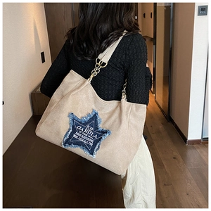 Detail of large beige suede tote with blue denim star patch and gold chain strap