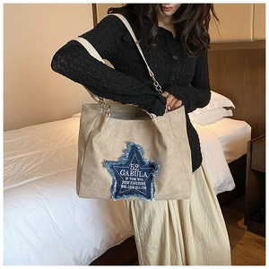 Close-up of beige suede tote bag featuring blue denim star patch and metal chain strap