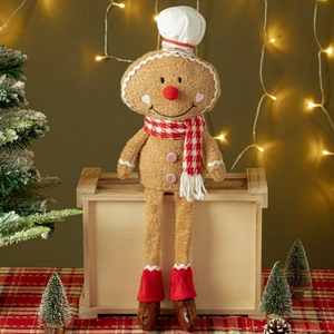 Plush gingerbread man chef doll with chef hat and scarf sitting in Christmas decor