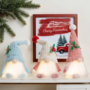 Three glowing Christmas gnomes with LED beards in blue, white, and pink on a festive shelf