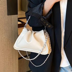 Chic beige cloud bag with pleated texture and chain strap worn by a model in a suit