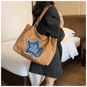 Close-up of brown suede tote bag featuring a navy star patch and gold chain strap