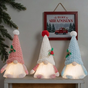 Three glowing Christmas gnomes with knit hats and LED lights on a white shelf