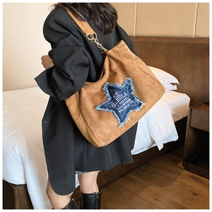 Detail of brown suede tote with blue denim star patch and gold chain strap