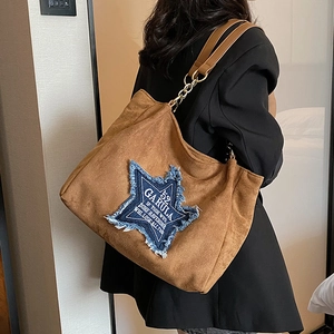 Brown suede tote bag with blue denim star patch shown worn on shoulder with chain strap