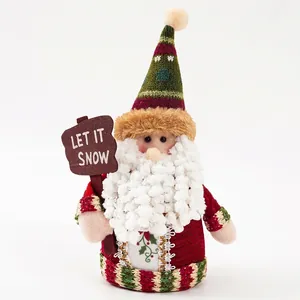 Christmas Santa plush doll with striped hat and wooden Let It Snow sign on white backdrop