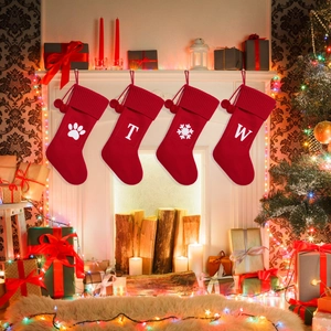 Detail of red knit Christmas stockings with white letters and snowflakes hanging by a fireplace