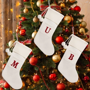 Close-up of cream knit Christmas stockings with red letters M, U, B on a festive tree