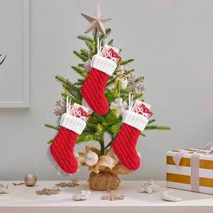 Tre calze di Natale rosse in maglia a trecce con risvolti bianchi su un albero