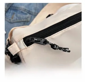 Detail of smooth black zipper with woven puller on cream nylon crossbody bag