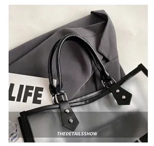 Detalle del bolso tote de PVC transparente con asa negra, remache plateado y hebilla metálica