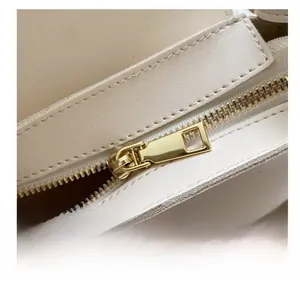Close-up of a smooth gold metal zipper and neat stitching on a cream leather bag