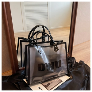 Detalle del bolso tote transparente con ribete de cuero negro y logo OWU sobre satén