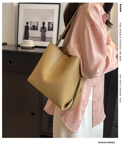 Close-up of light brown leather bucket bag styled with a pink silk shirt and long strap