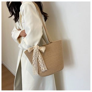 Detail view of woven shoulder bag featuring a delicate cream lace bow on the side