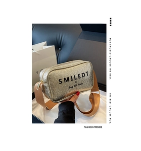 Detail of golden textured crossbody bag featuring wide fabric strap and branded lettering