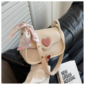 Cream shoulder bag with pink heart patch and floral scarf detail on a leather sofa